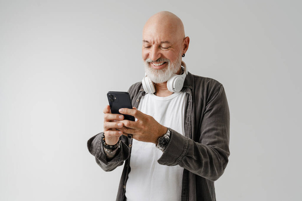 Bald european man with headphones using mobile phone isolated over white background - Foto, immagini
