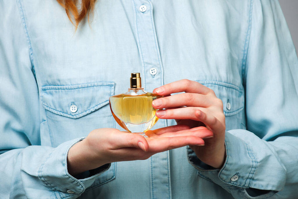 Woman dressed in a blue denim shirt holds bottle of perfume in her hands - Foto, afbeelding