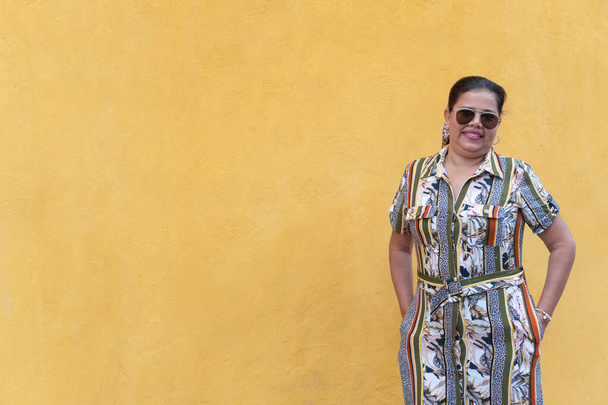 Latin nő egy ruha és napszemüveg áll szemben a sárga fal - Fotó, kép