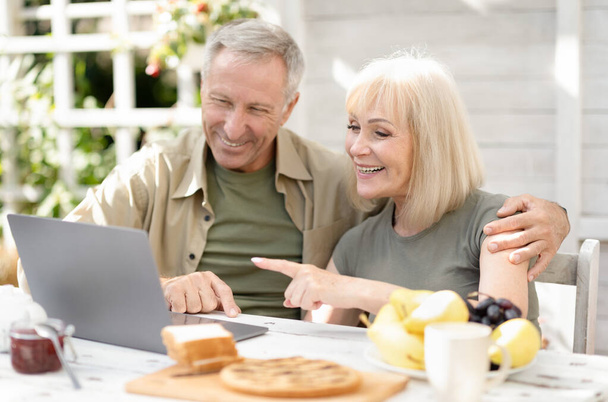 Сучасна концепція пенсійного способу життя. Щаслива старша пара, використовуючи ноутбук та Інтернет, сидить на відкритому повітрі
 - Фото, зображення