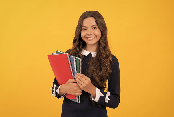 счастливый ребенок держит в руках школьные тетради для домашнего обучения на желтом фоне, школа - Фото, изображение