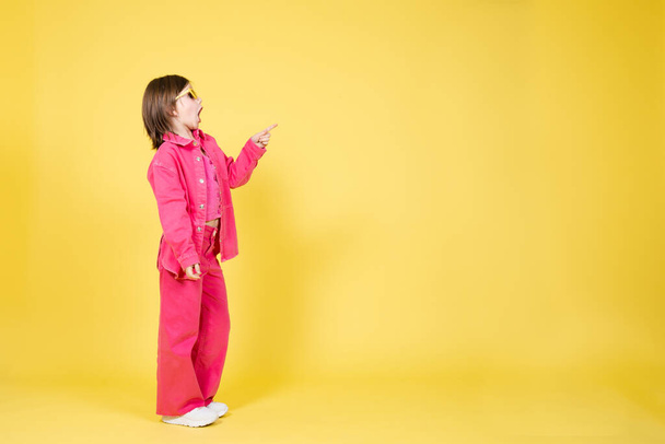 Ganzkörperporträt des niedlichen kleinen Mädchens zeigt auf Kopierraum isoliert auf gelbem Kopierraum - Foto, Bild
