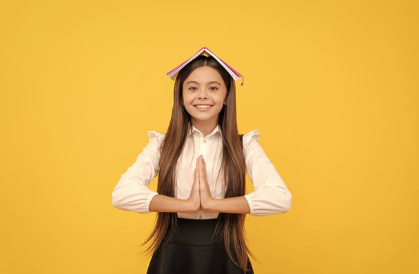 glücklich Teenie-Mädchen in Schuluniform mit Buch auf dem Kopf meditiert mit Handbewegung, ruhig bleiben - Foto, Bild