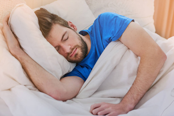 Спит по выходным. Обрезанный снимок красивого молодого человека, спящего в постели дома. - Фото, изображение