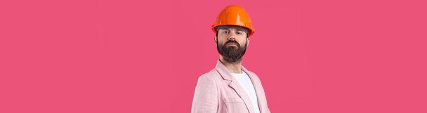 Portré fiatal építőmérnök visel narancs kemény kalap, egy rózsaszín kabát álló piros stúdió háttér. - Fotó, kép