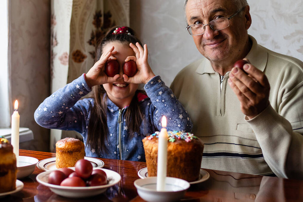Щасливий літній чоловік дідусь готується до Великодня з онучкою. розмальовані кольорові яйця на Великдень
 - Фото, зображення