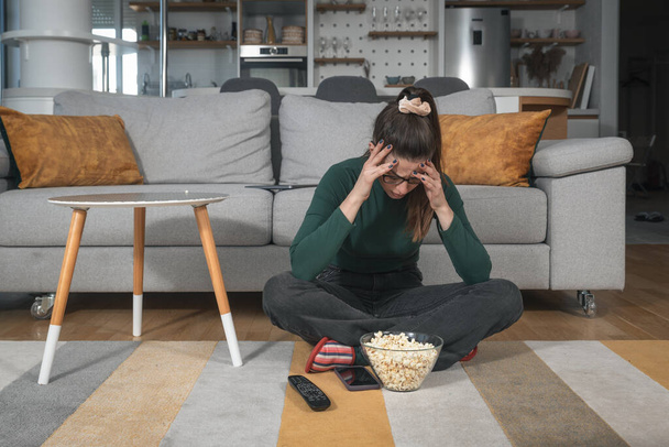 Young shocked vegetarian woman sitting at home watching television changing the program after she saw animal brutality. Unhappy female with disgusting facial expression pressing tv remote button. - Foto, Imagem