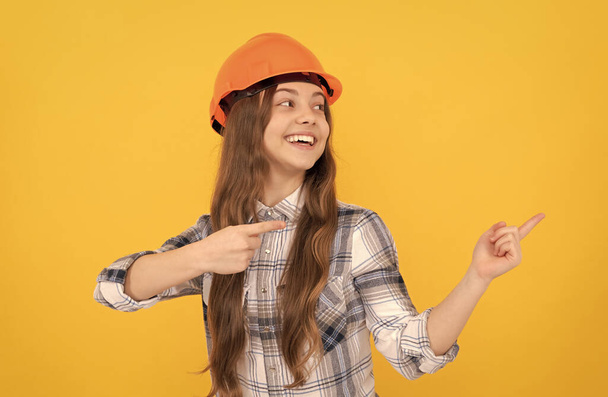 Счастливая девочка-подросток в шлеме и рубашке, указывающая пальцем на пространство для копирования, рекламирует - Фото, изображение