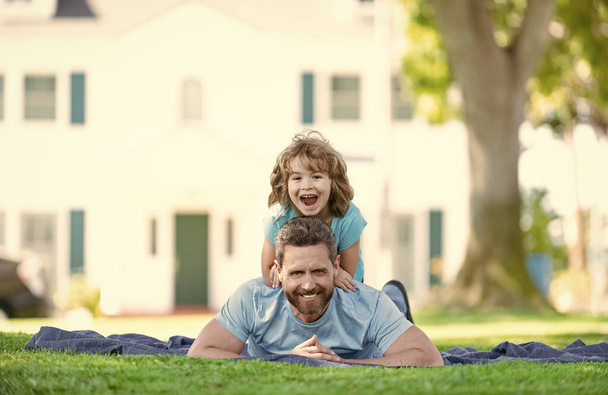 Happy son kid ride fathers back relaxing on blanket laid on grass summer outdoors, fun - Photo, Image