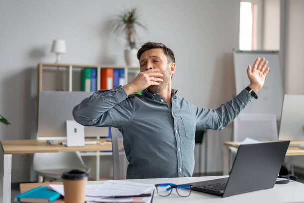 Ospalý dospělý podnikatel zívá, unavený z práce s laptopem v kanceláři, mužský workoholik pocit ospalosti nebo znuděný - Fotografie, Obrázek
