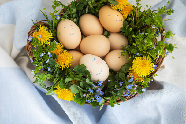 Beautiful spring bouquet in a wooden basket with Easter painted eggs, eggs with cute faces - Photo, Image