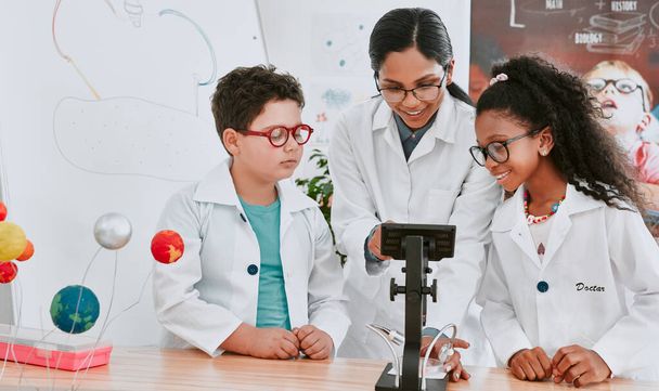 Lets take a closer look at this. Shot of a young science teacher using a microscope with her pupils in science class at school. - 写真・画像