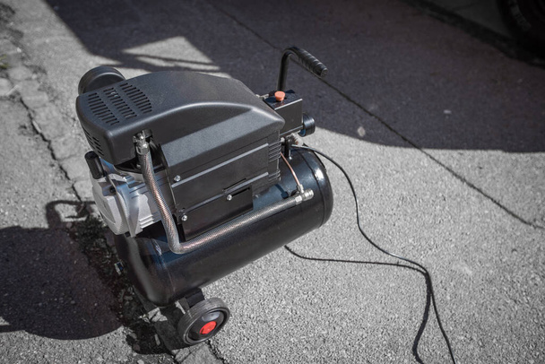Small hobby air compressor used to pump tires or other inflatable dings, resting on a sidewalk of a town road. - 写真・画像