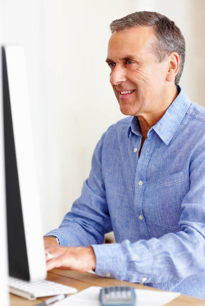 Sonriente hombre maduro calculando los gastos usando la computadora. Retrato de un hombre maduro sonriente calculando los gastos usando la computadora. - Foto, imagen