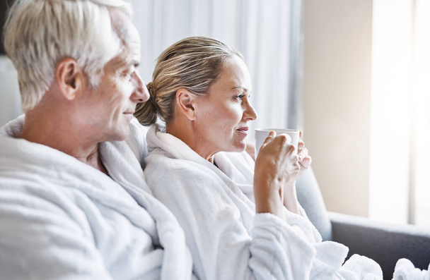 What a great day for relaxing. Shot of a cheerful middle aged couple relaxing together while wearing bathrobes and sitting on a couch inside of a spa during the day. - Fotografie, Obrázek