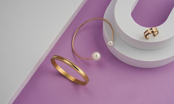 Top view of golden with pearls bracelet and ring on white podium on purple background - 写真・画像