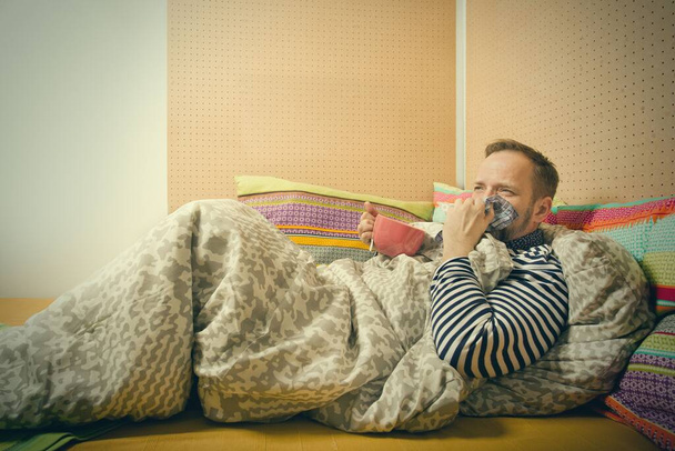 Mature sick man drinking hot tea from cup alone at home in bed - Foto, Imagem