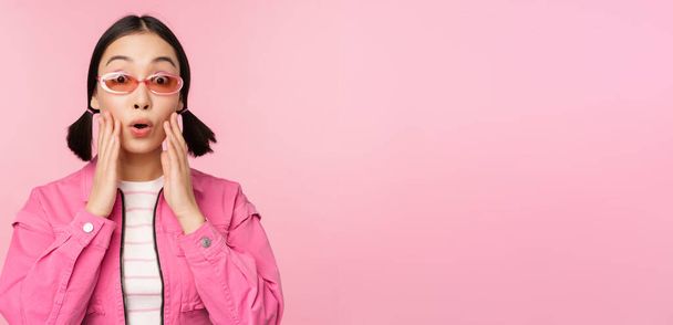 Immagine di ragazza asiatica che sembra sorpresa ed eccitata, sorridente, reazione stupita alle grandi notizie, in piedi su sfondo rosa - Foto, immagini