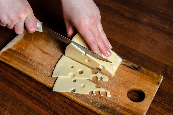 Slicing cheese on a wooden board - Fotoğraf, Görsel