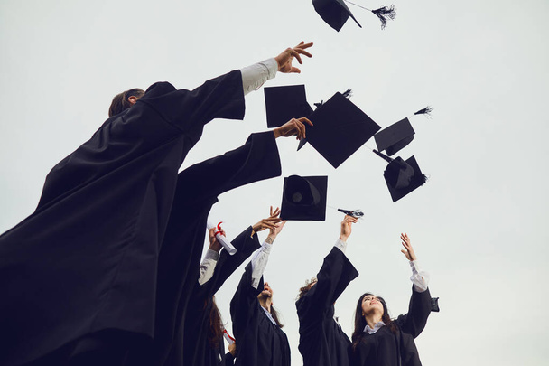 Afgestudeerden gooien hun academische hoeden in de lucht tijdens een plechtige ceremonie op de universiteit. - Foto, afbeelding