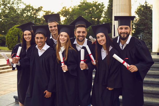 Group of happy graduates walking with dimplomas in raised hands over university building background - Fotoğraf, Görsel