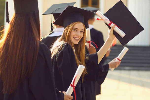 Smiling beautiful girl university or college graduate standing with diploma and looking at camera - Φωτογραφία, εικόνα