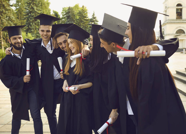 Group of smiling university graduates standing with diplomas, hugging each other - Φωτογραφία, εικόνα