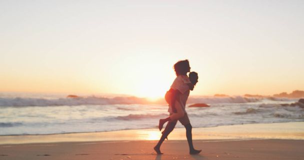 We renden weg naar de zonsondergang. Volledige opname van een aanhankelijk jong paar dat een wandeling maakt op het strand bij zonsondergang. - Foto, afbeelding