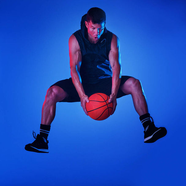 Gram, żeby wygrać. Niebieskie filtrowane ujęcie sportowca grającego w koszykówkę w studio. - Zdjęcie, obraz