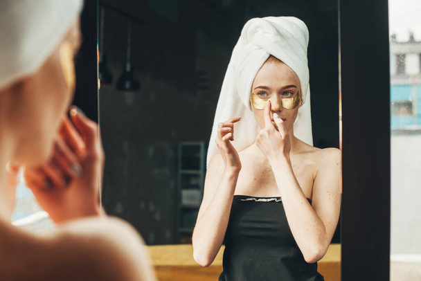 Beautiful caucasian woman applying under eyes patches, removing dark circles and puffiness, looking at herself in mirror. Under concept eye treatment and body - Photo, Image