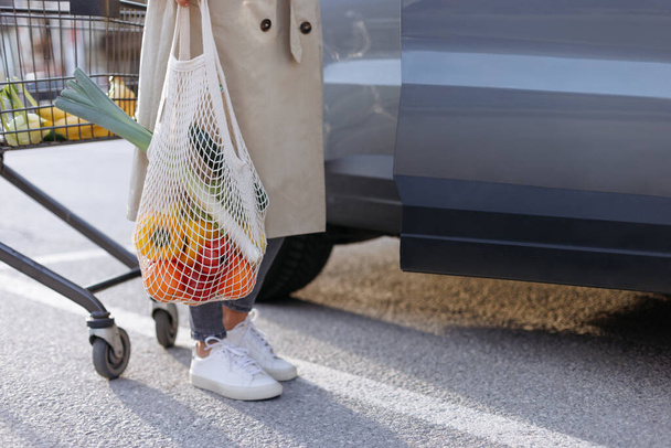 Girl holding mesh shopping bag with organic fruits and vegetables. Zero waste, plastic free concept - Fotoğraf, Görsel