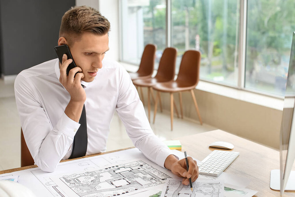 Young male landscape designer talking by mobile phone while working in office - Photo, Image