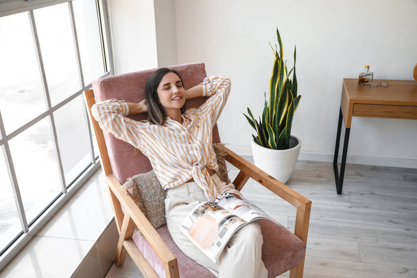 Fiatal nő magazin ül kényelmes karosszék otthon - Fotó, kép