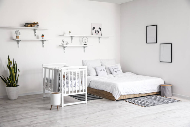 Modern interieur van gezellige kamer met groot bed en comfortabele babybedje - Foto, afbeelding