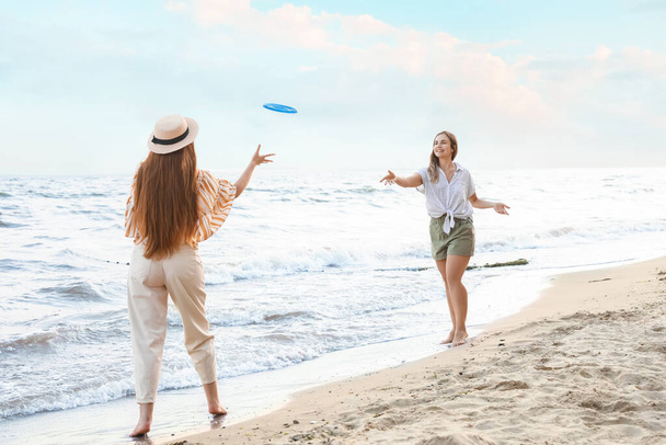 Happy young women playing frisbee on sea beach - Foto, imagen