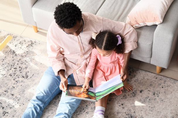 Onnellinen afroamerikkalainen mies ja hänen pieni tyttärensä lukemassa kirjaa kotona, ylhäältä - Valokuva, kuva