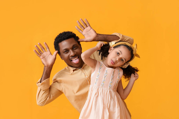 Portrait of funny little African-American girl and her father on yellow background - Photo, Image