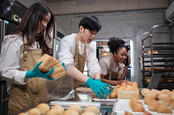 Three young friends and startup partners of bread dough and pastry foods busy with homemade baking jobs while cooking orders online, packing, and delivering on bakery shop, small business entrepreneur. - Photo, Image