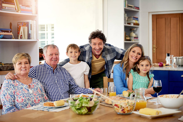 Goede tijden staan altijd op het menu bij familiebijeenkomsten. Portret van een multi-generationele familie genietend van een maaltijd samen thuis. - Foto, afbeelding