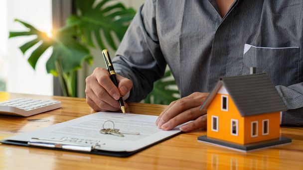 Businessman's signature on documents, checks, and documents in real estate investment projects on the desk. Sales report on the mortgage agent market in real estate concepts. - Photo, Image