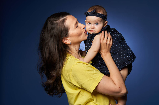 Young mother having a great time with her baby daughter, studio shot over blue background - Fotó, kép