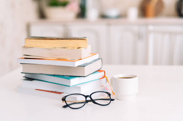 Stack of books with glasses and cup of coffee standing on table - Photo, Image