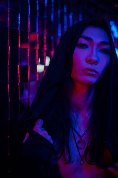 Nahaufnahme Porträt eines androgenen Modells in einer Kapuze. Männliche Transgender im Studio mit Neonlicht. - Foto, Bild
