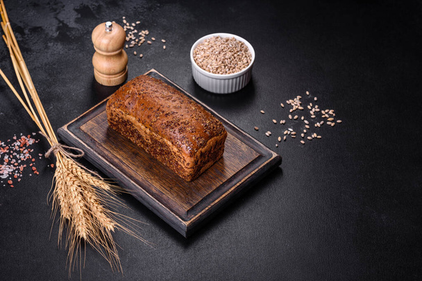 Fresh baked brown bread with ears and grains of wheat on a dark concrete background - Photo, Image