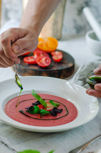 Bowl of tomato soup with basil on white background. Cold pink tomato soup. Restaurant supply. The chef decorates the dish. - Foto, Imagem