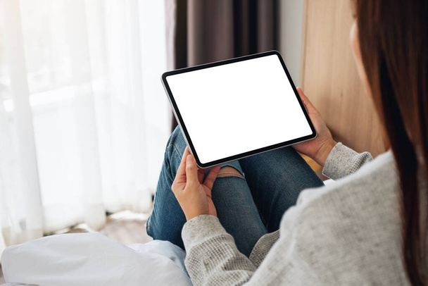 Mockup kép egy nő kezében fekete tabletta pc üres asztali fehér képernyő, miközben ül egy hangulatos fehér ágy otthon - Fotó, kép