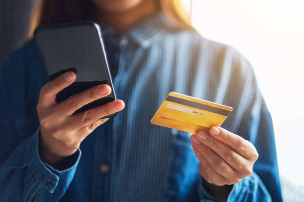 Close-up beeld van een jonge vrouw met kredietkaart voor de aankoop en online winkelen op de mobiele telefoon - Foto, afbeelding