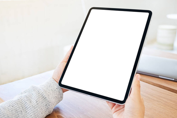 Mockup image of a woman holding black tablet pc with blank white screen on wooden table - Photo, Image