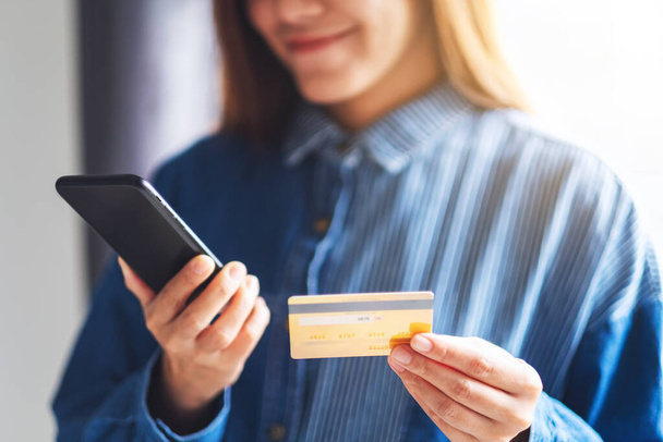 Closeup image of a young woman using credit card for purchasing and shopping online on mobile phone - 写真・画像