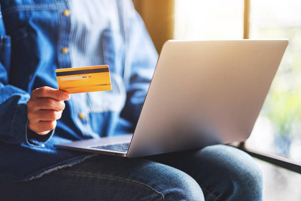 Nahaufnahme einer Frau, die Kreditkarten hält, während sie einen Laptop benutzt - Foto, Bild
